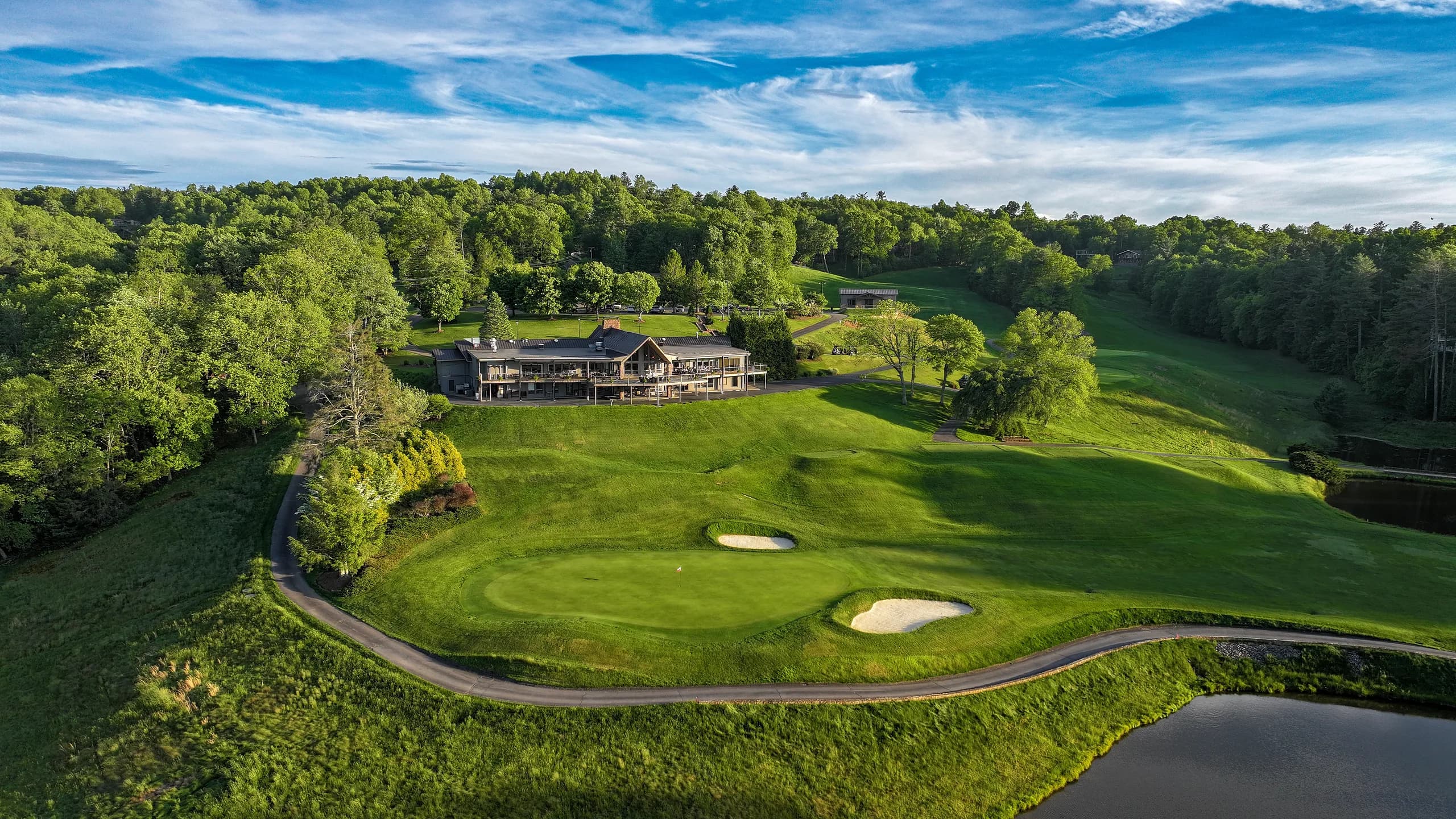 Golden-hour aerial of a ridge-top clubhouse above a bunkered green